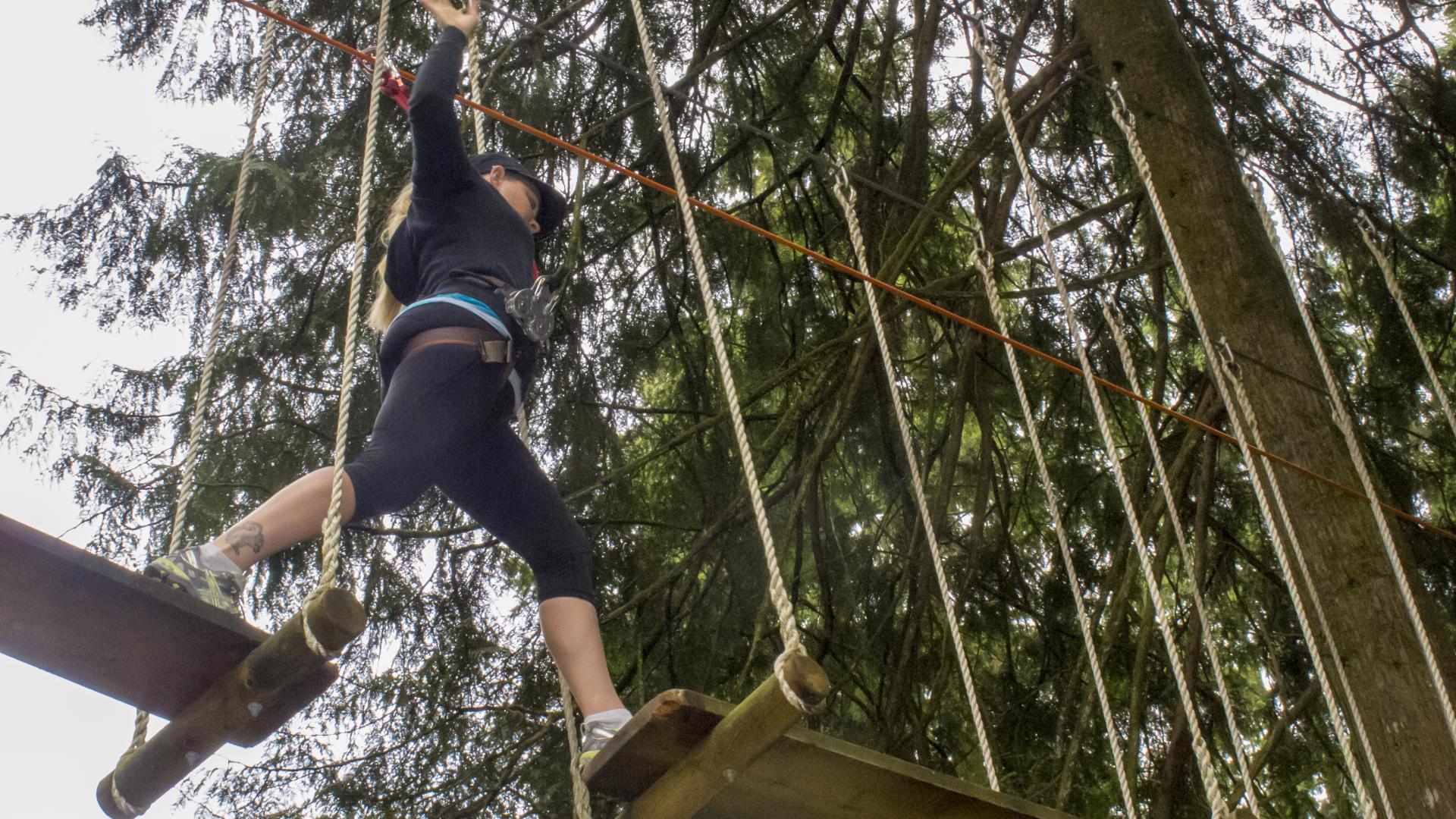 Seen from below, a woman walk across a bridge of suspended wood boards.